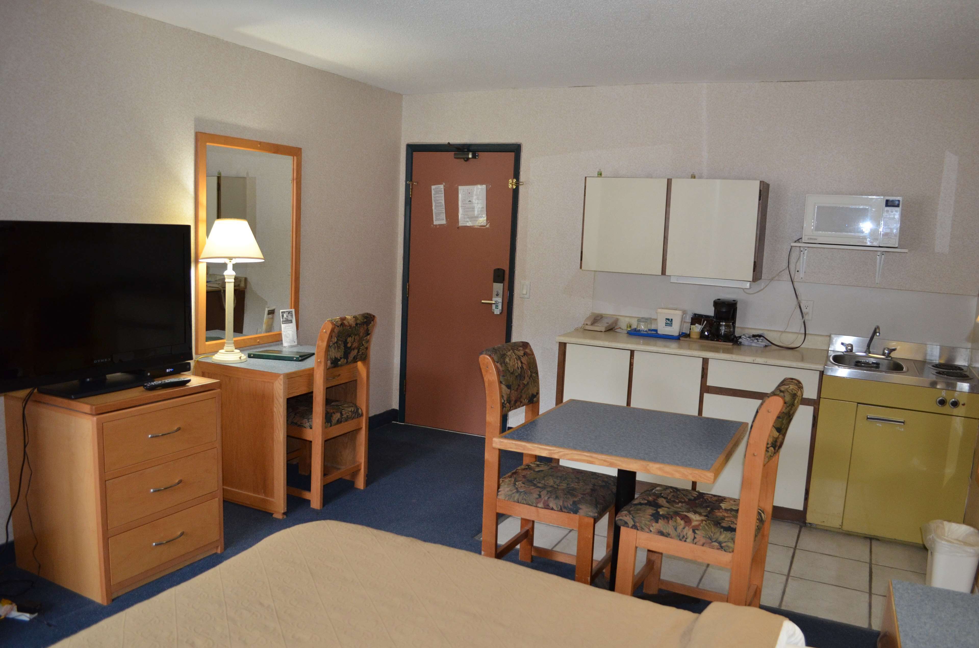 A hotel room with a bed, a desk with a chair, a television, a microwave, and a small kitchenette.