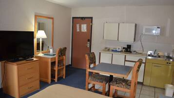 A hotel room with a bed, a desk with a chair, a television, a microwave, and a small kitchenette.