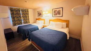 Habitación de hotel con dos camas individuales, cabeceros de madera, una mesita de noche pequeña, una lámpara, un cuadro enmarcado en la pared y una ventana con cortinas.