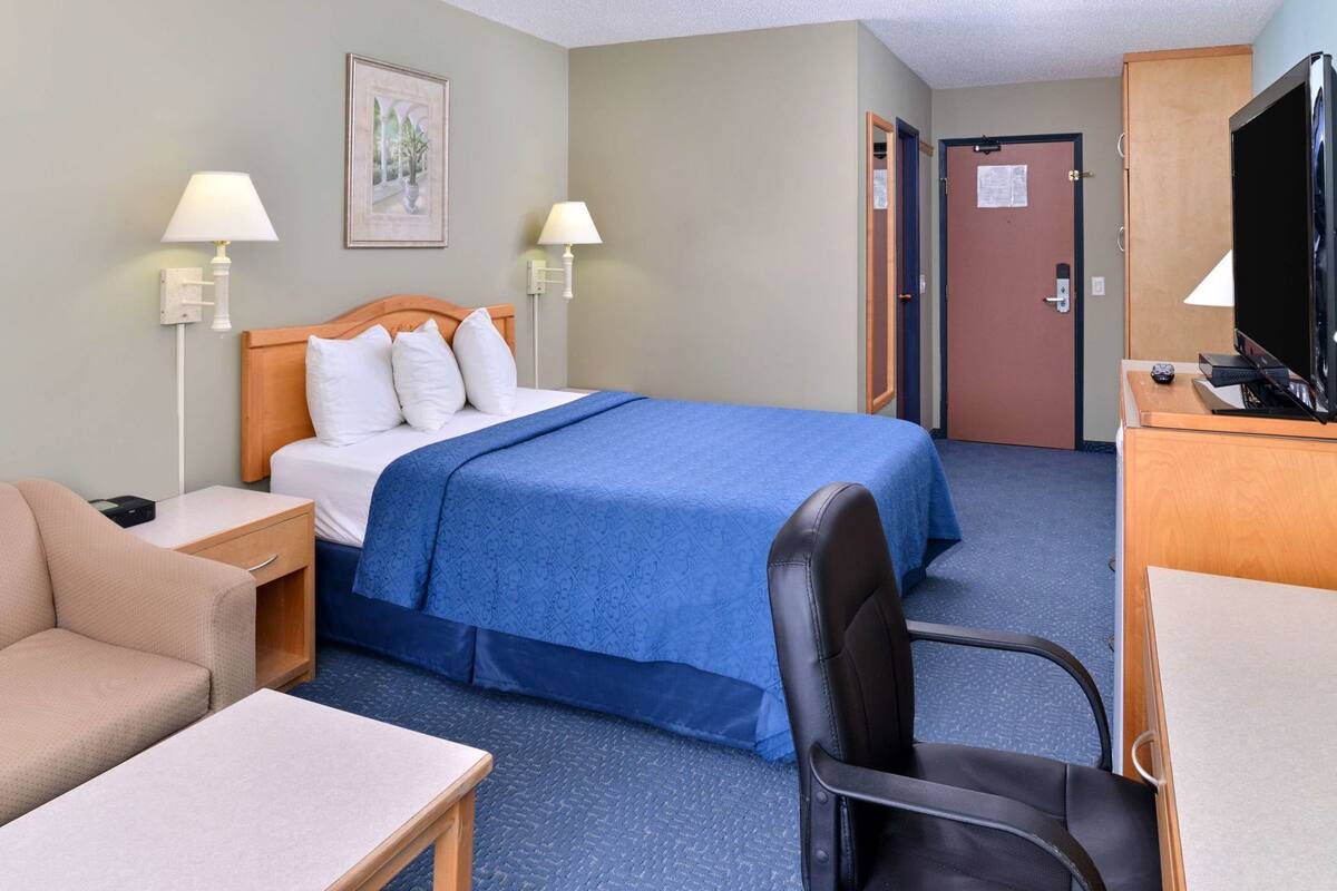 A hotel room with a bed, a desk, a chair, a TV, and two lamps.