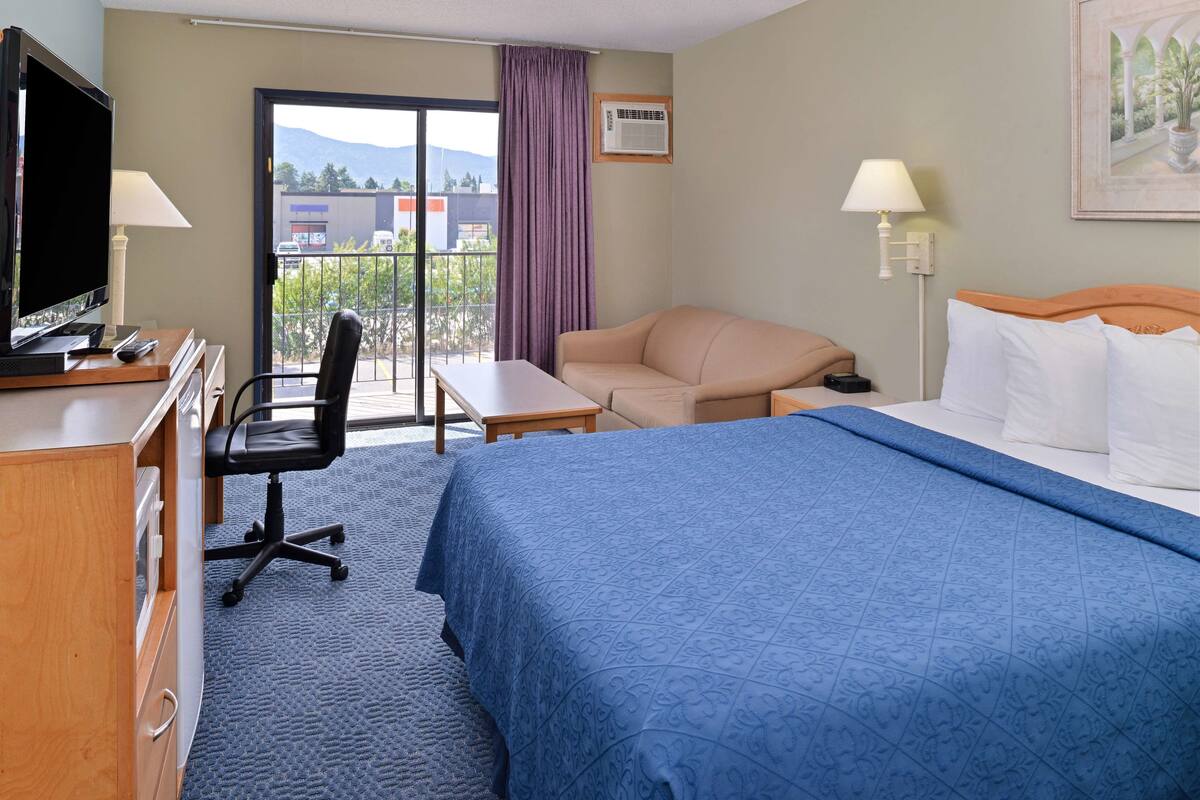 A hotel room with a bed, a desk, a chair, a television, and a view of the outdoors.