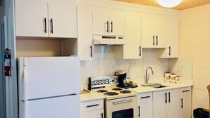 A compact kitchen with white cabinets, a built-in oven, a stove, and a refrigerator. - Canadas Best Value Inn & Suites Castlegar (Castlegar)