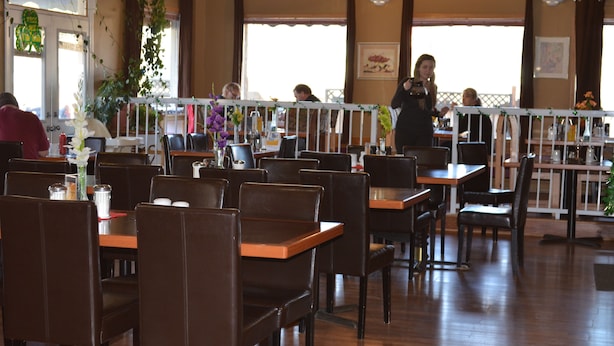 Un restaurante con mesas y sillas de madera, una barandilla blanca y ventanas amplias.