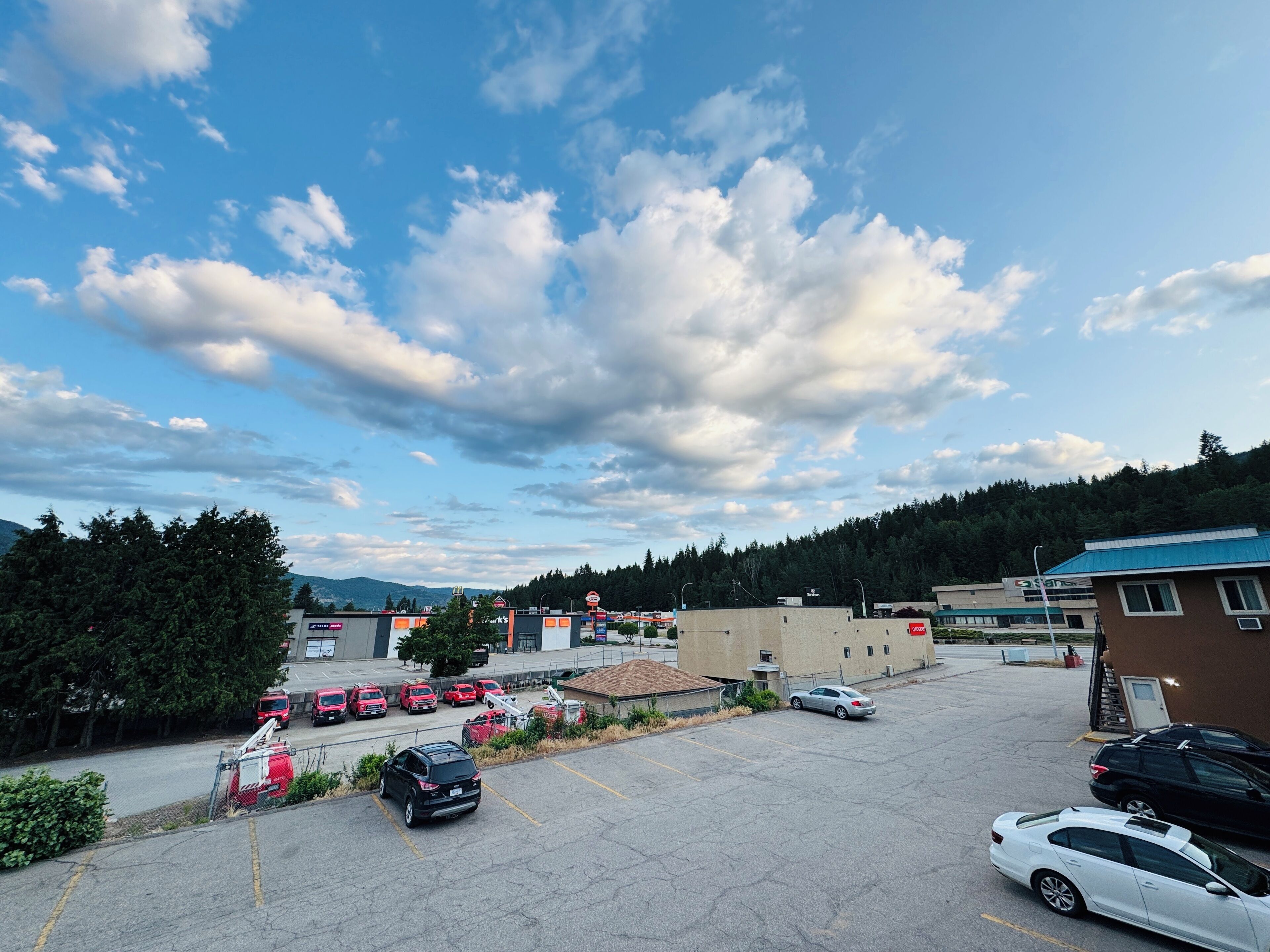 A parking lot with several cars, a building with a blue roof, and a mountainous background.