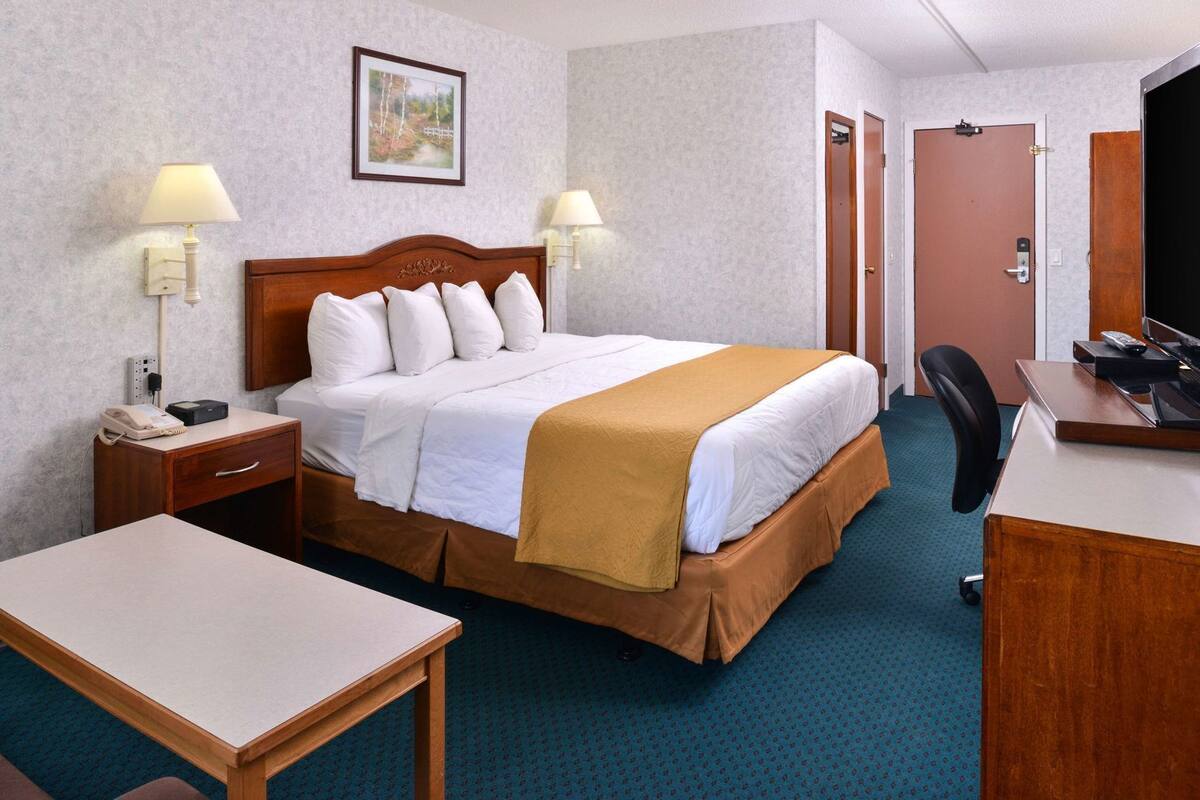 A hotel room with a bed, bedside tables, a desk, a chair, and a television.