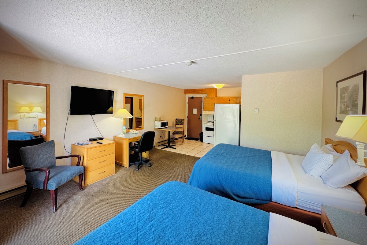 A hotel room with two beds, a desk, a chair, a television, a microwave, and a refrigerator.
