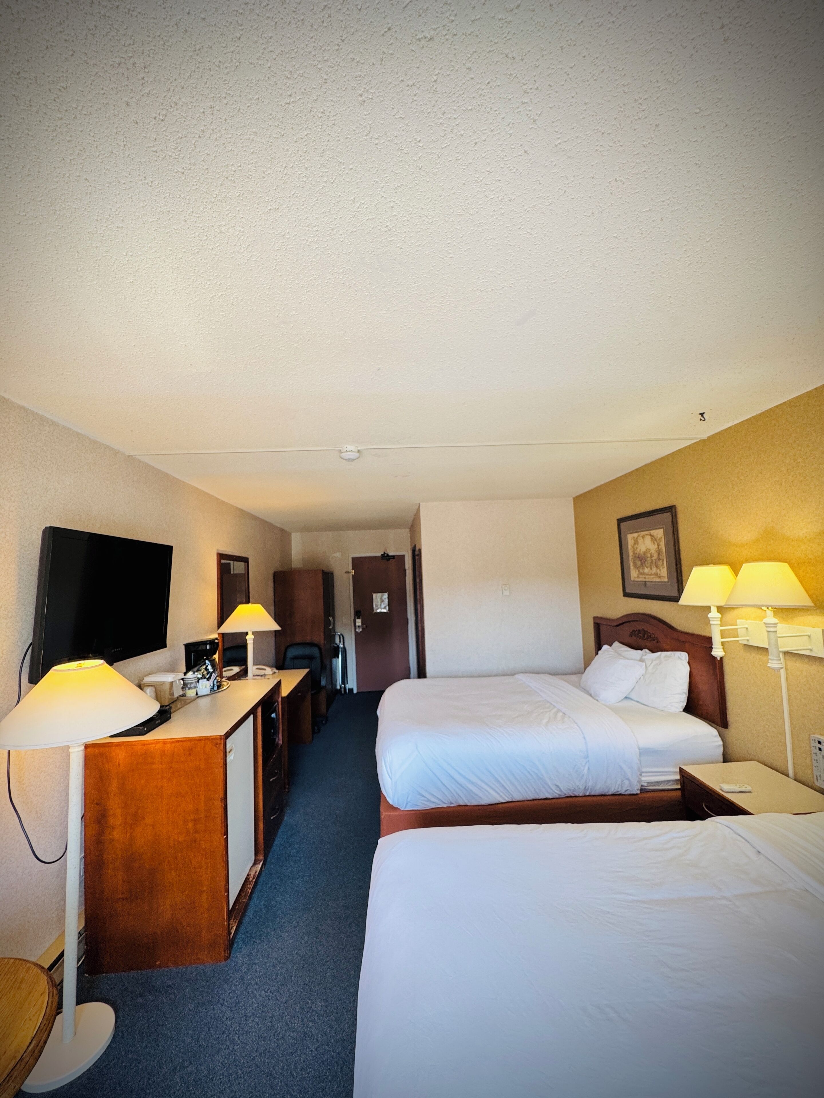 Habitación de hotel con dos camas, un escritorio con lámpara, televisión y puerta que da a otra habitación.