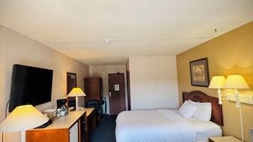 Habitación de hotel con dos camas, un escritorio con lámpara, televisión y puerta que da a otra habitación.