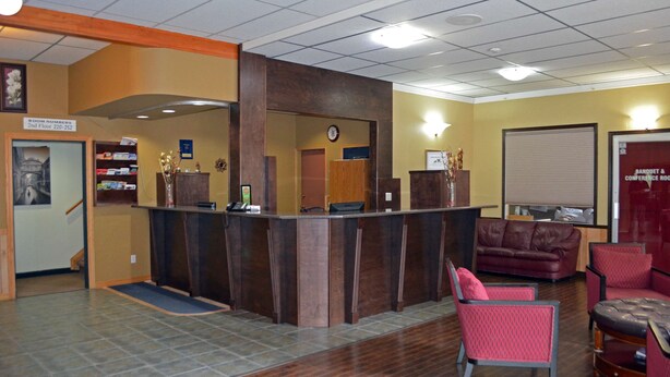 A reception area with a wooden reception desk, a clock, a red couch, and a sign indicating room numbers on the 2nd floor. - Canadas Best Value Inn & Suites Castlegar (Castlegar)