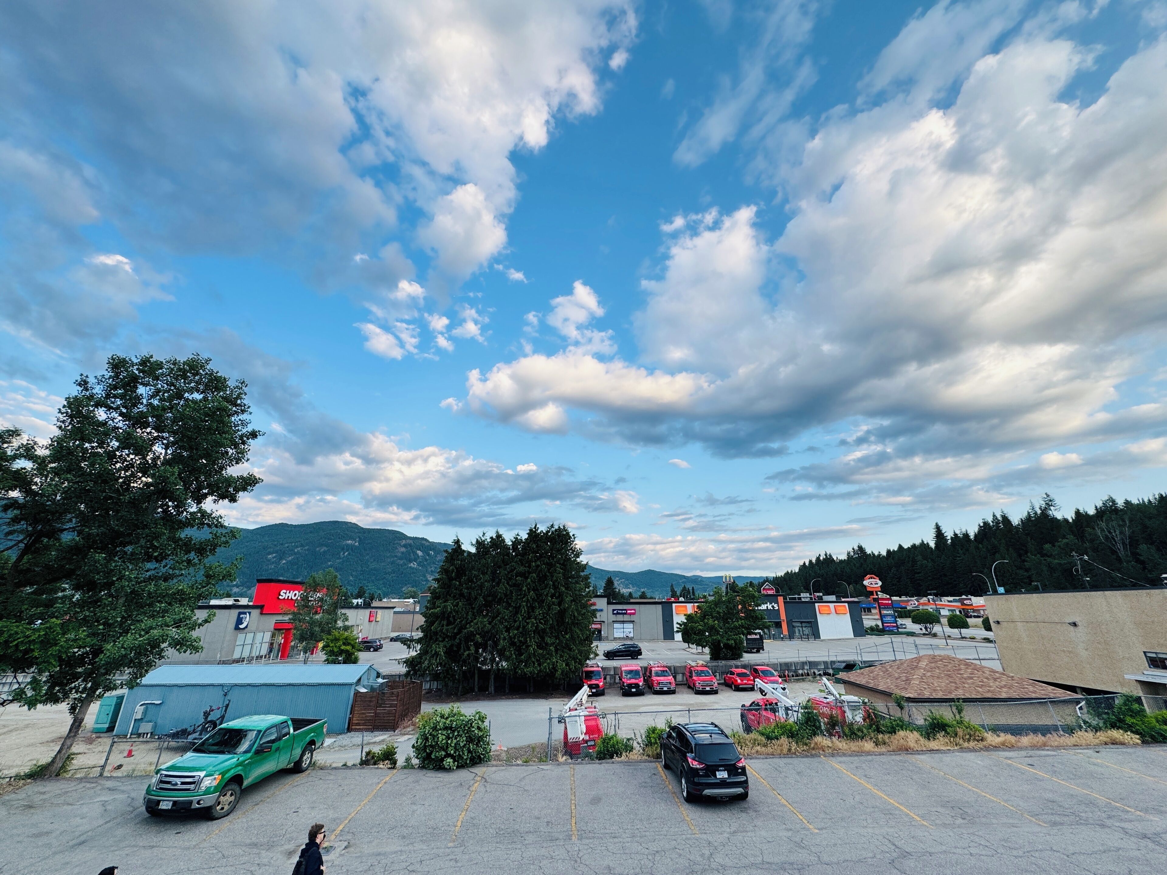 A parking lot with several cars, a green truck, and a building with a red sign.