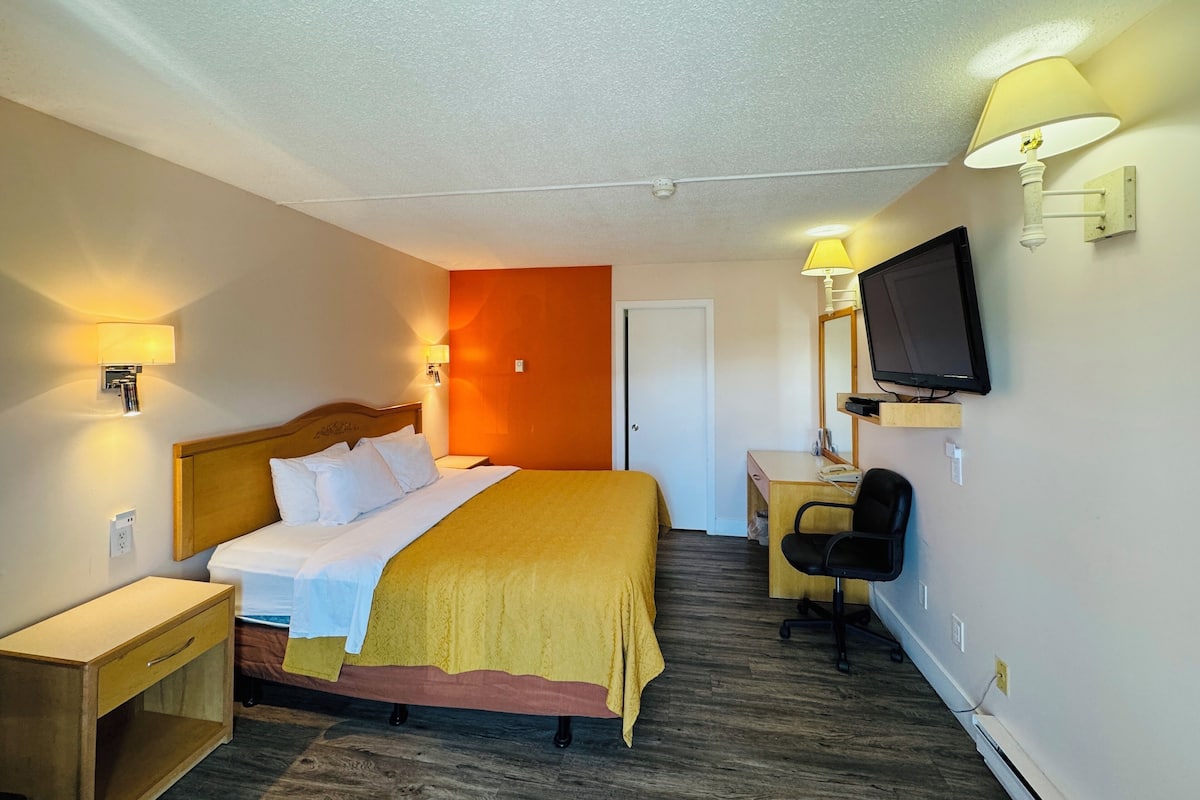 A hotel room with a bed, bedside table, chair, desk, lamp, and television.