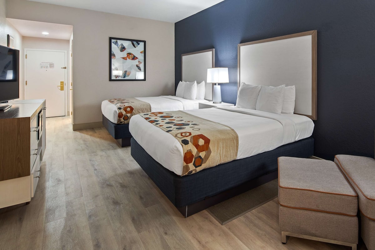 A hotel room with two beds, a desk, and a chair.