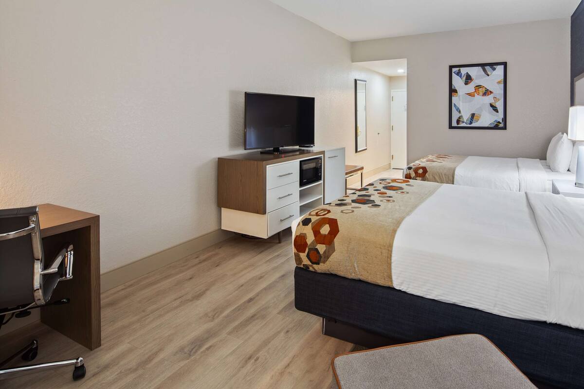 A hotel room with a bed, a desk, a chair, a television, and a bathroom visible through an open door.
