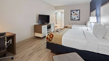 Habitación de hotel con cama, escritorio, silla, televisor y baño visible a través de una puerta abierta.