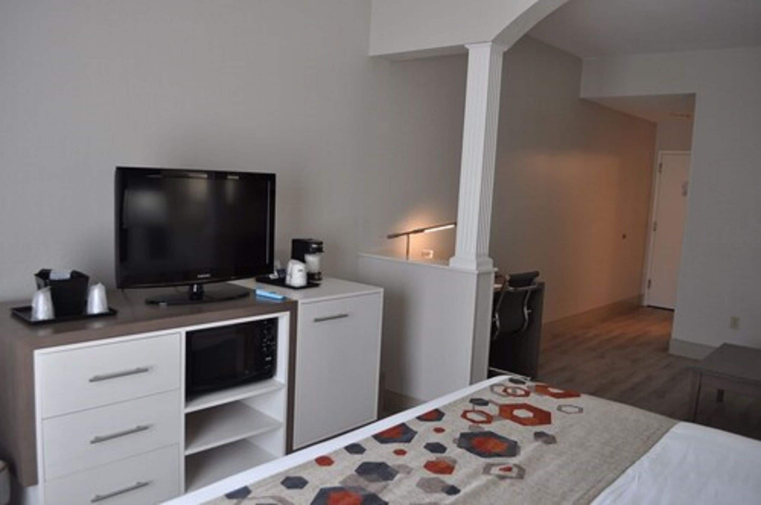 A hotel room with a bed, a TV, a coffee machine, and a desk with drawers.
