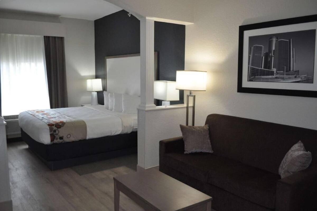 A hotel room with a bed, a sofa, two bedside lamps, a framed picture on the wall, and a window with curtains.