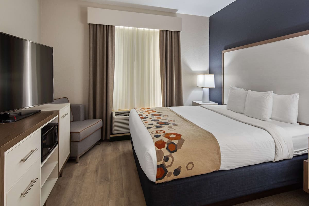 A hotel room with a large bed, bedside tables, a flat-screen TV, a desk with a computer, and a window with curtains.