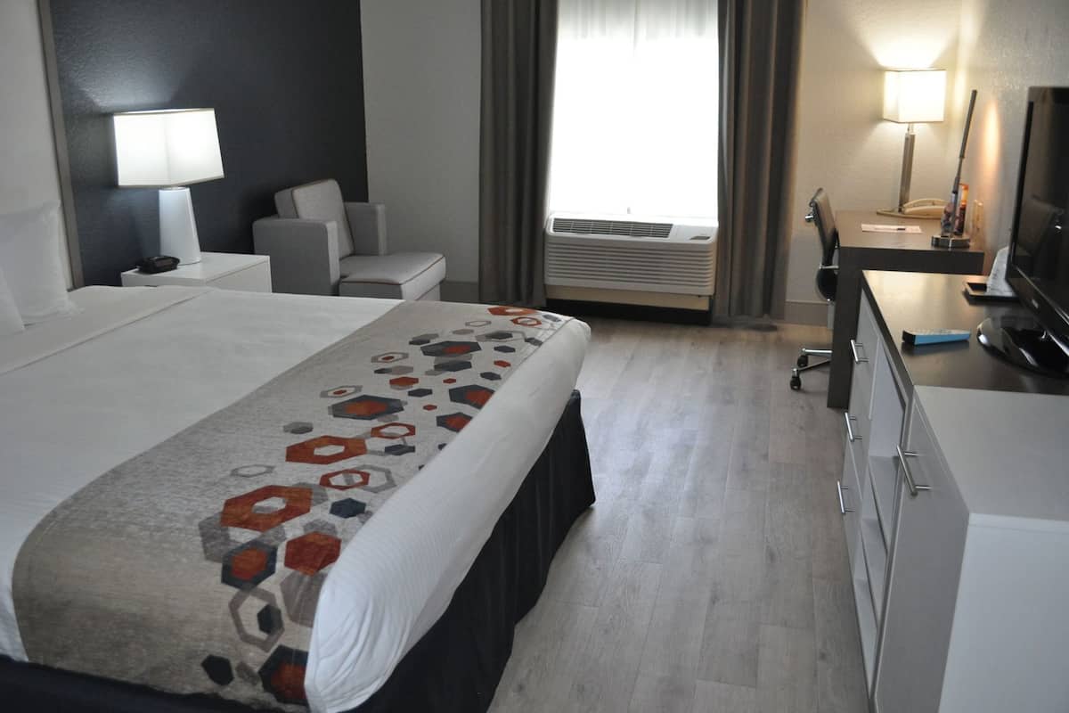 A hotel room with a bed, a desk, a chair, a TV, and an air conditioning unit.