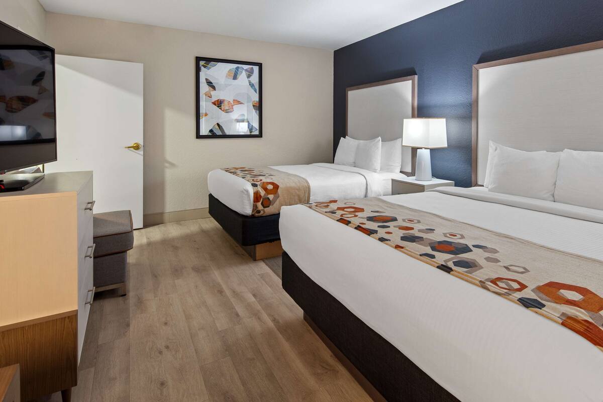 A hotel room with two beds, a desk, a chair, a TV, and a painting on the wall.