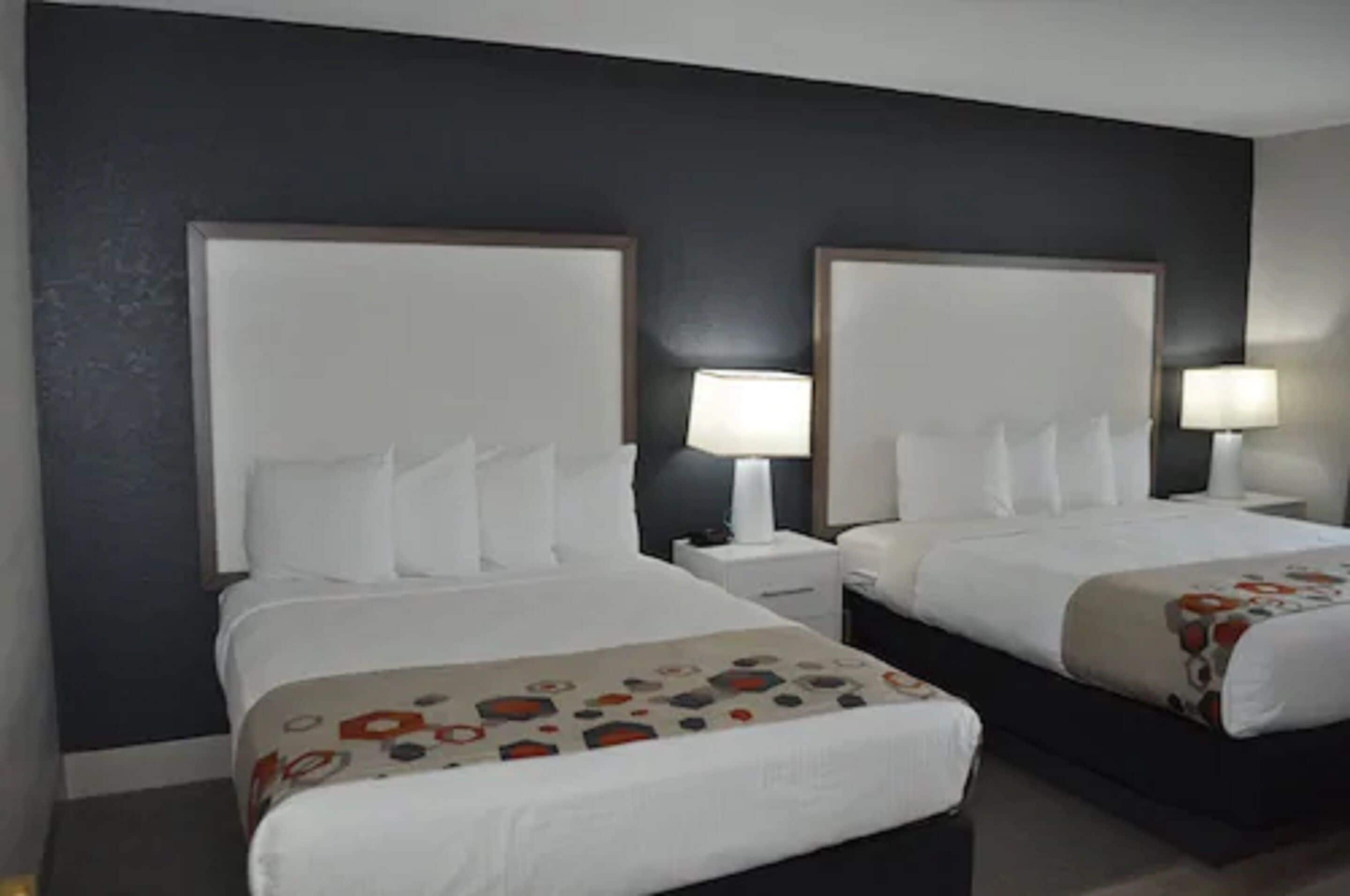 A hotel room with two beds, each with a white headboard and a bedside table with a lamp.
