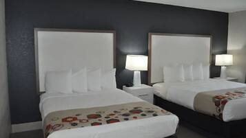 A hotel room with two beds, each with a white headboard and a bedside table with a lamp.