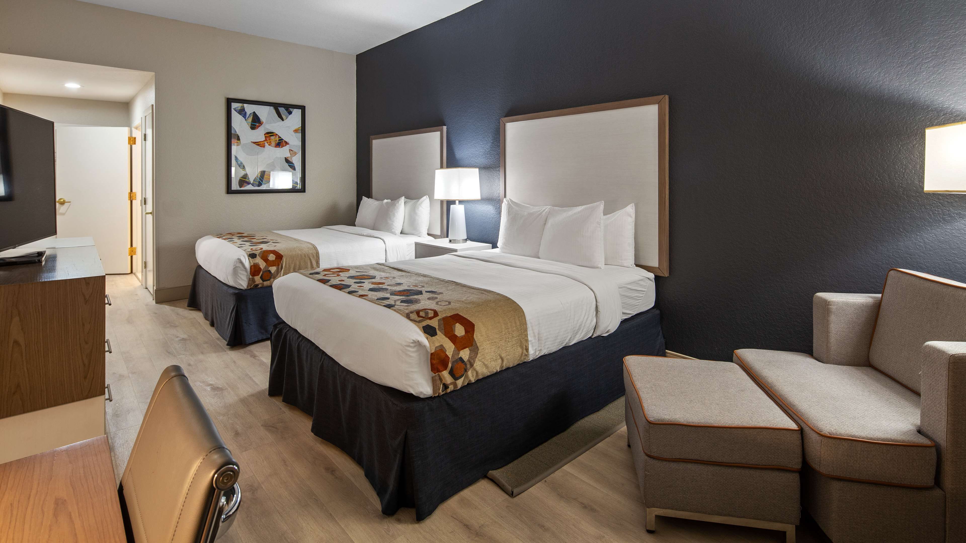 A hotel room with two beds, a desk, a chair, and a TV.