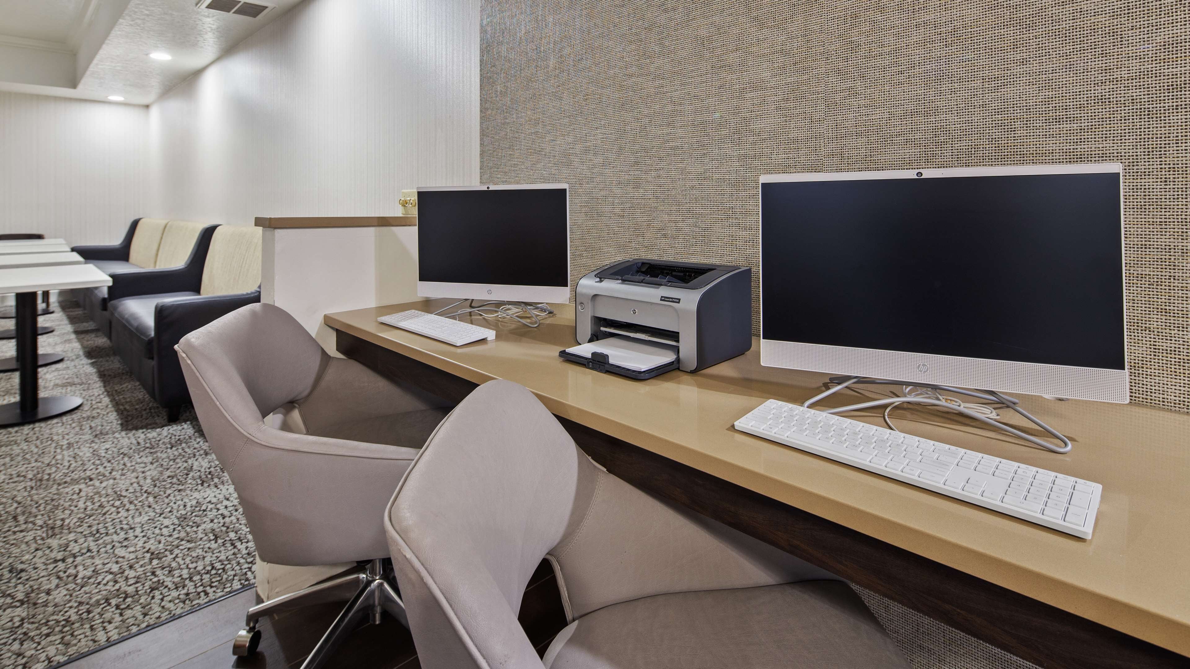 A modern office space with two desktop computers, a printer, and a keyboard on a wooden desk.