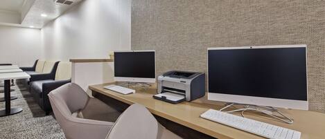 A modern office space with two desktop computers, a printer, and a keyboard on a wooden desk.