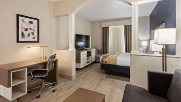 Habitación de hotel con escritorio, silla, televisor, cama y un espejo grande.
