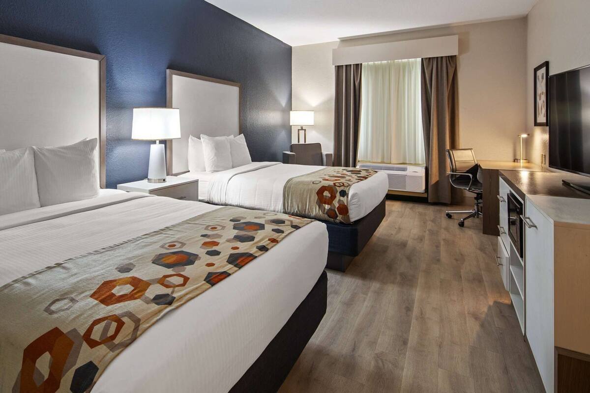 A hotel room with two beds, a desk, a TV, and a window with curtains.