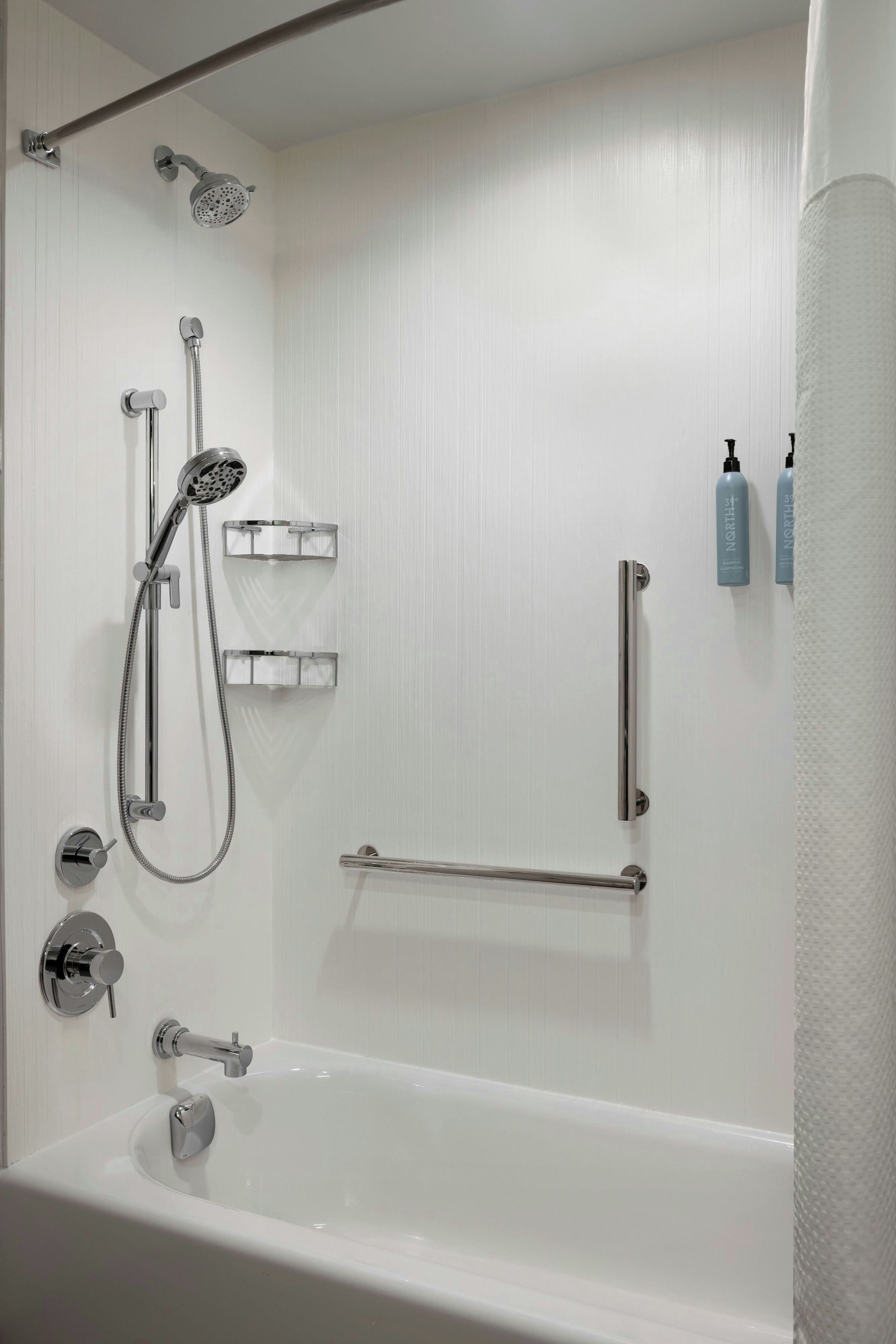 Un baño moderno con una bañera, ducha con cabezal de ducha manual, toallero y dos botellas de champú en la pared.