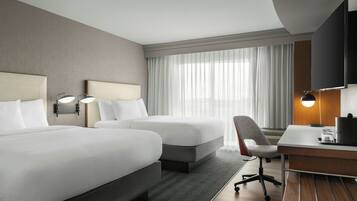 Ein Hotelzimmer mit zwei Betten, einem Schreibtisch, einem Stuhl, einem Fernseher und einem Fenster mit Vorhängen.