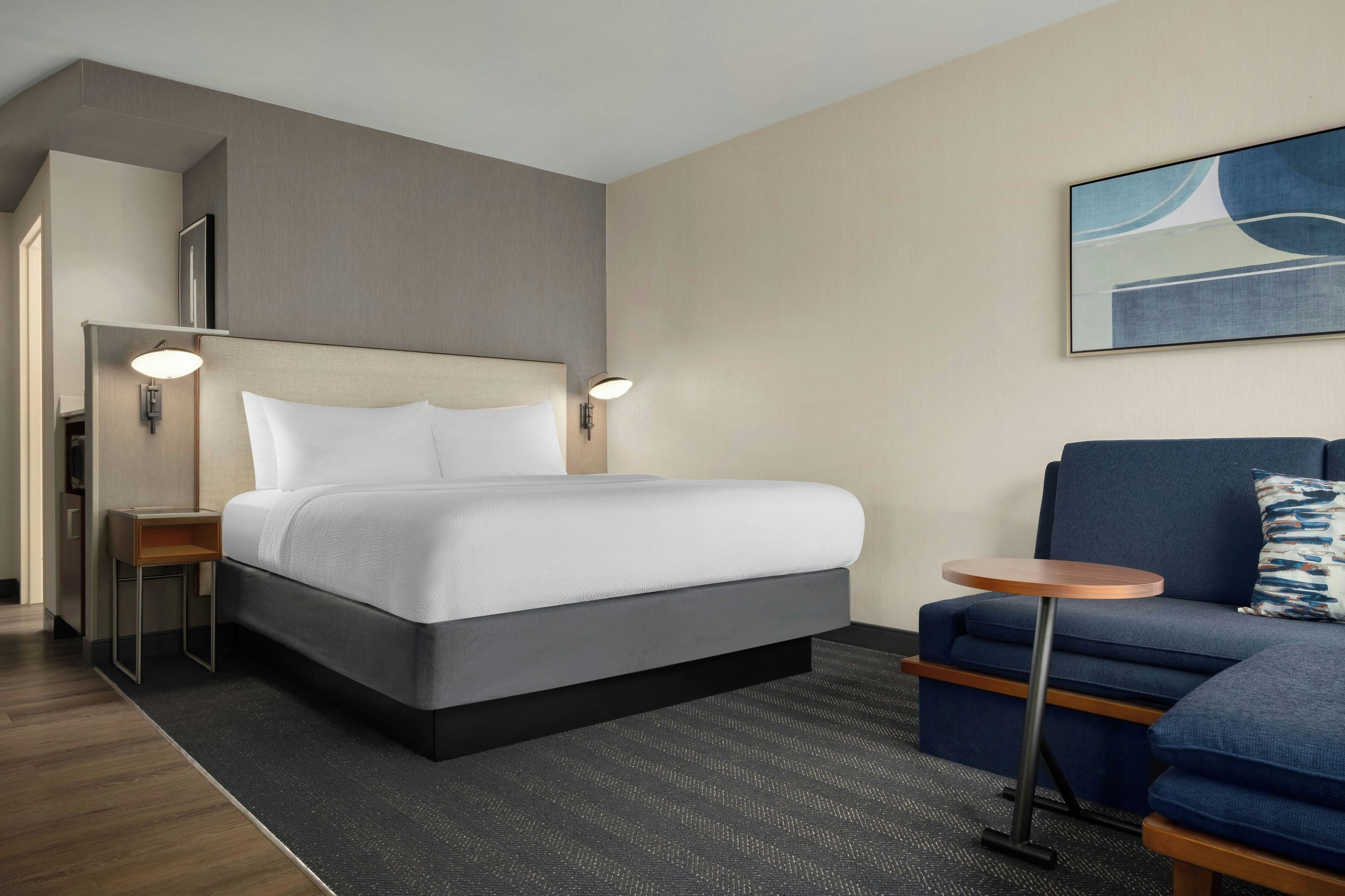 A hotel room with a bed, a small round table, a sofa, and a painting on the wall.