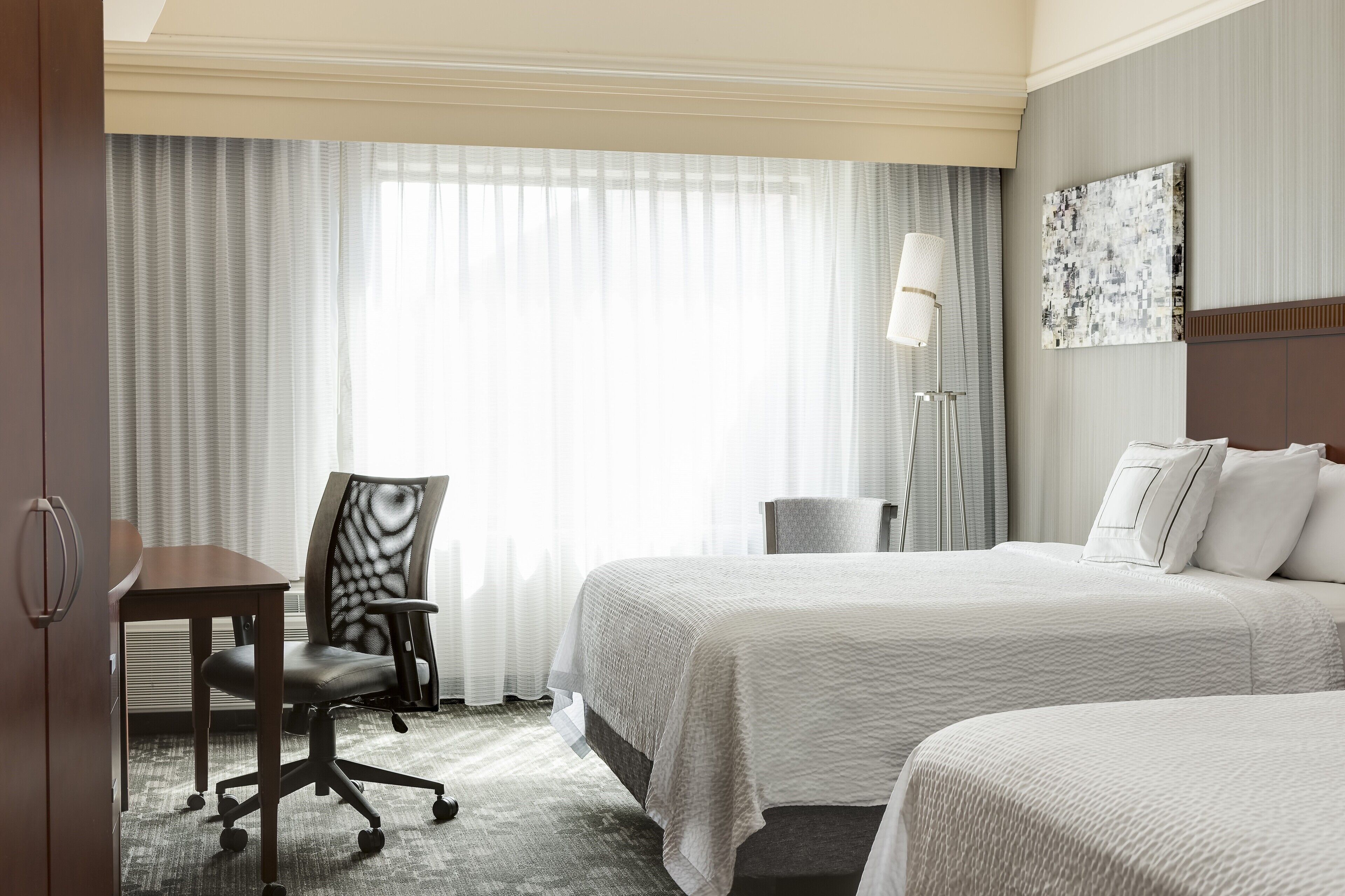 Une chambre d’hôtel avec deux lits, un bureau, une chaise et une lampe.