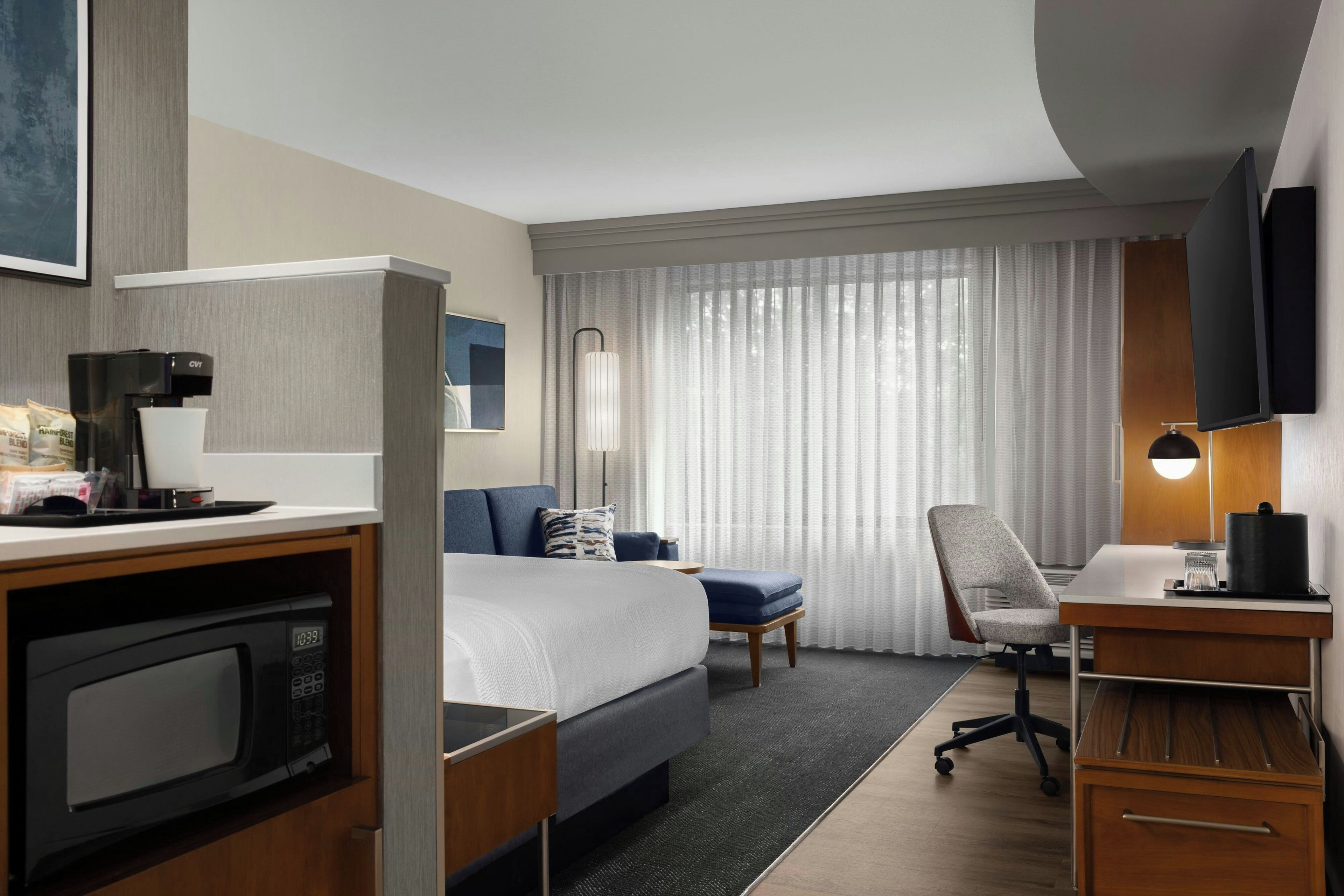 A hotel room with a bed, desk, chair, and a television.