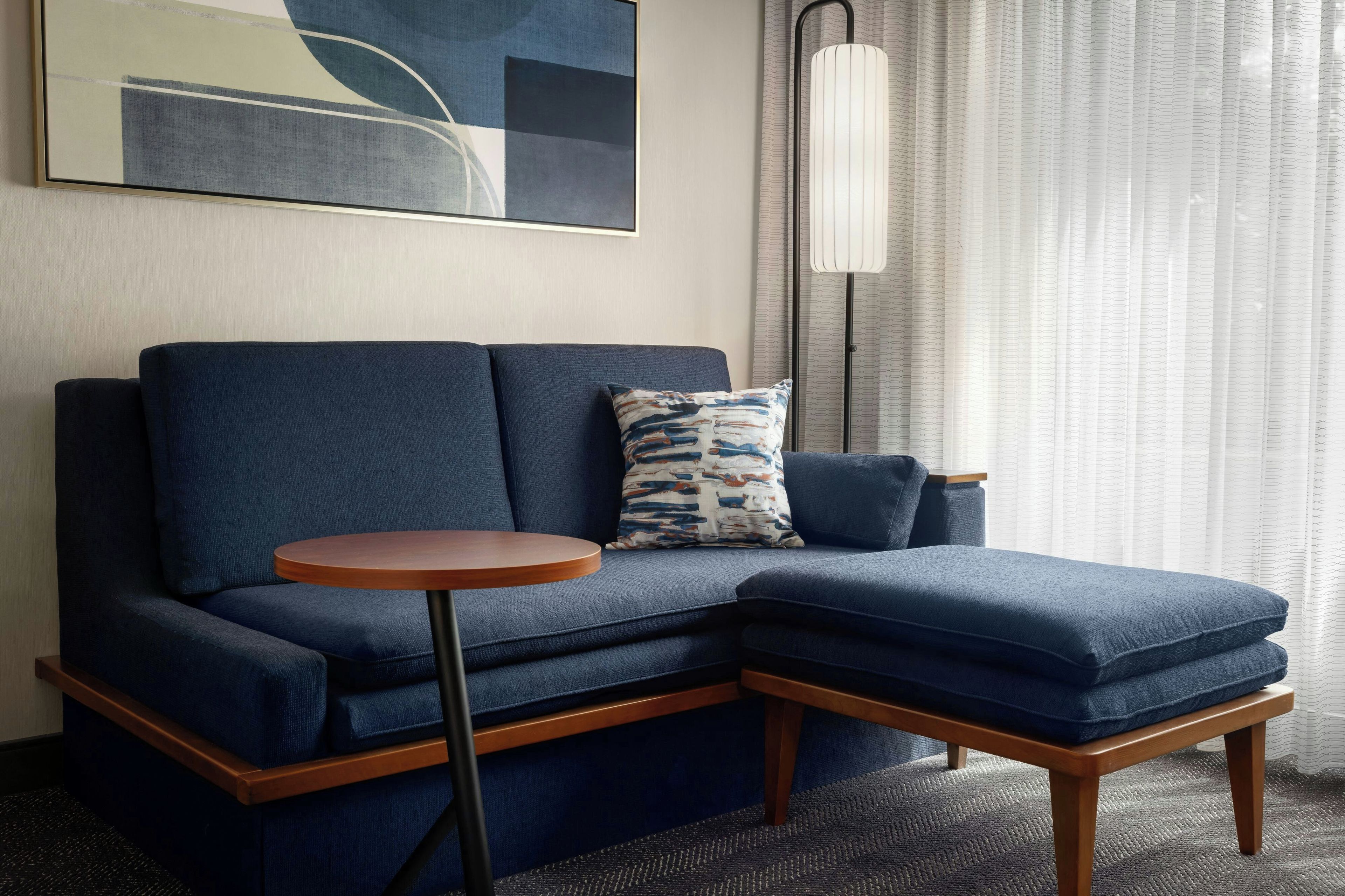 A modern living room with a sectional sofa, a small round wooden table, and a floor lamp.