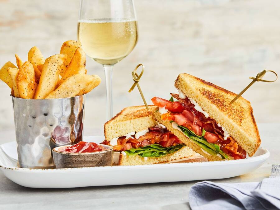 Un plato con un sándwich a la plancha, una copa de vino blanco y un recipiente de kétchup.
