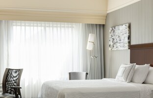 Una habitación de hotel con cama, una silla, una lámpara de pie y un cuadro en la pared.