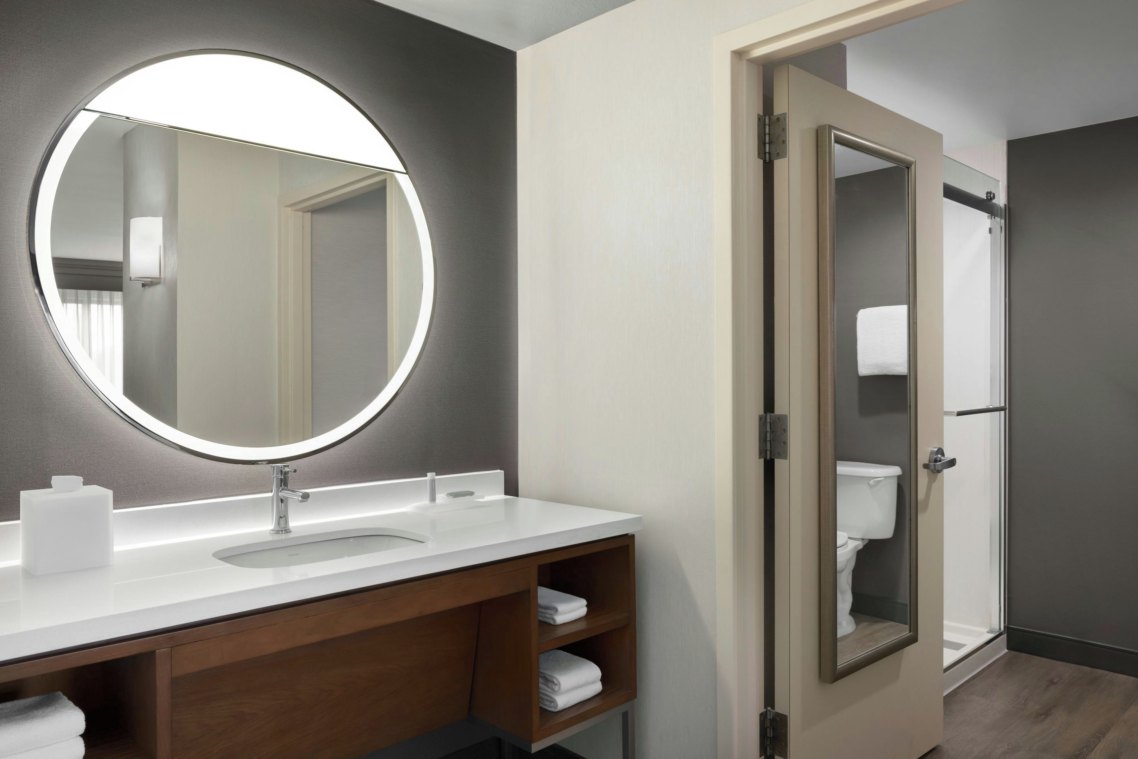 Un baño moderno con un espejo redondo, un lavabo y un inodoro.