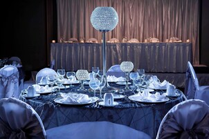 Una mesa de comedor formal, decorada con cristalería, platos y servilletas, y un centro de mesa de cristal decorativo.