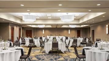 A conference room with multiple round tables, each set with white tablecloths and chairs, and a patterned carpet.