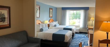 A hotel room with two beds, a sofa, a table, and a lamp.