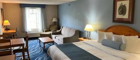 A hotel room with a bed, a desk, a chair, a lamp, and a window.