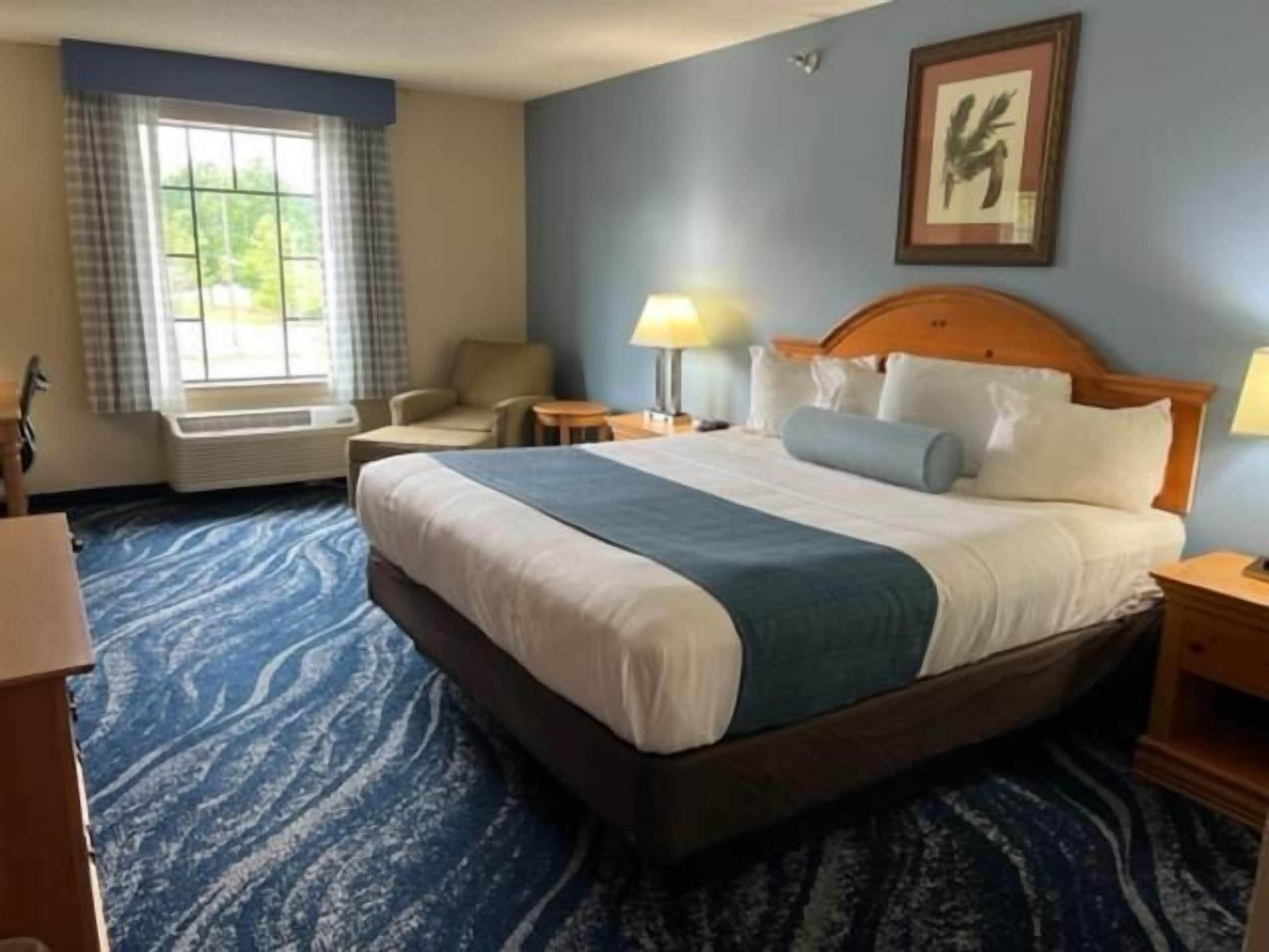 Une chambre d’hôtel avec un grand lit, une chaise, un bureau et une fenêtre avec des rideaux.