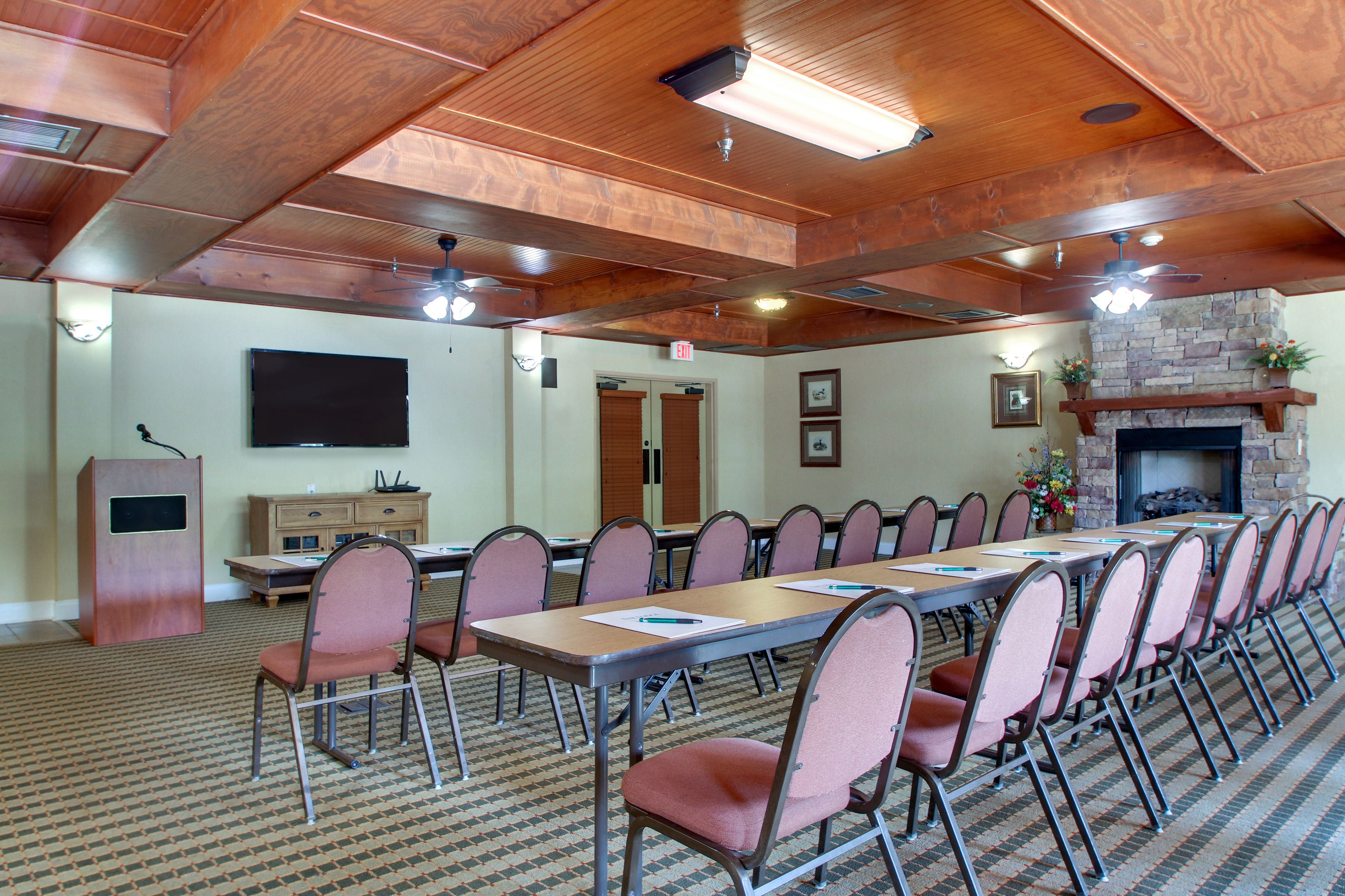 A conference room with a long table, chairs, a fireplace, and a television on the wall.