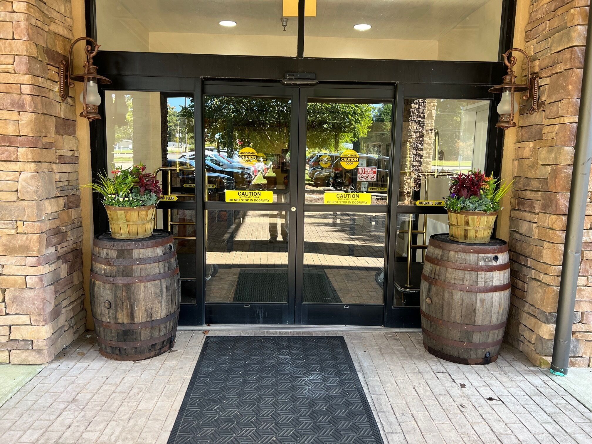 A building entrance with a black door, two wooden barrels, and potted plants.