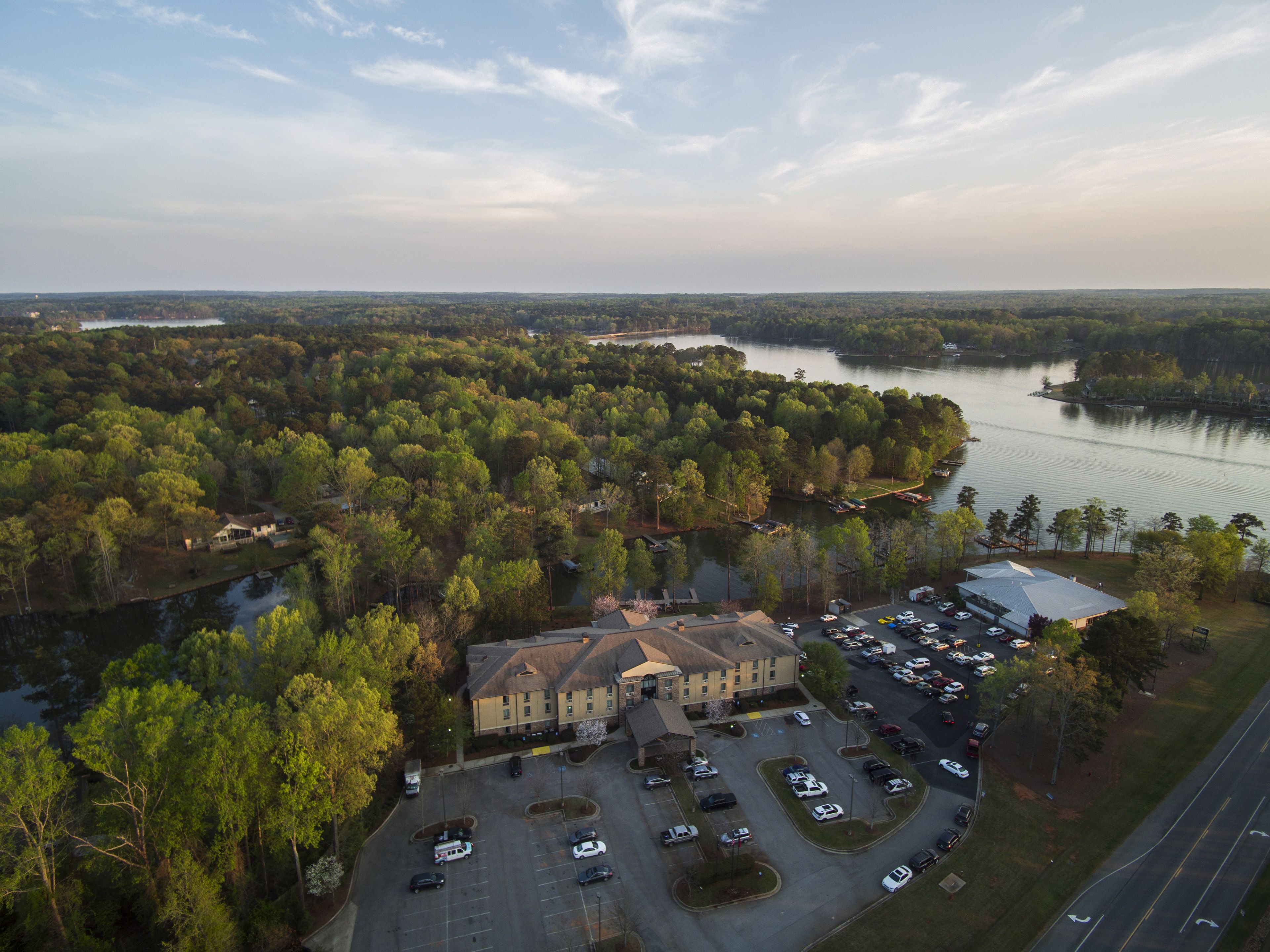 Luchtbeeld van een hotel met een parkeerplaats, omringd door dicht bos en een meer.