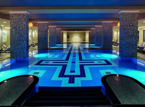 Una piscina interior moderna amb un mosaic de relleus geomètrics, envoltada d'llits de solàrium i una escala central.
