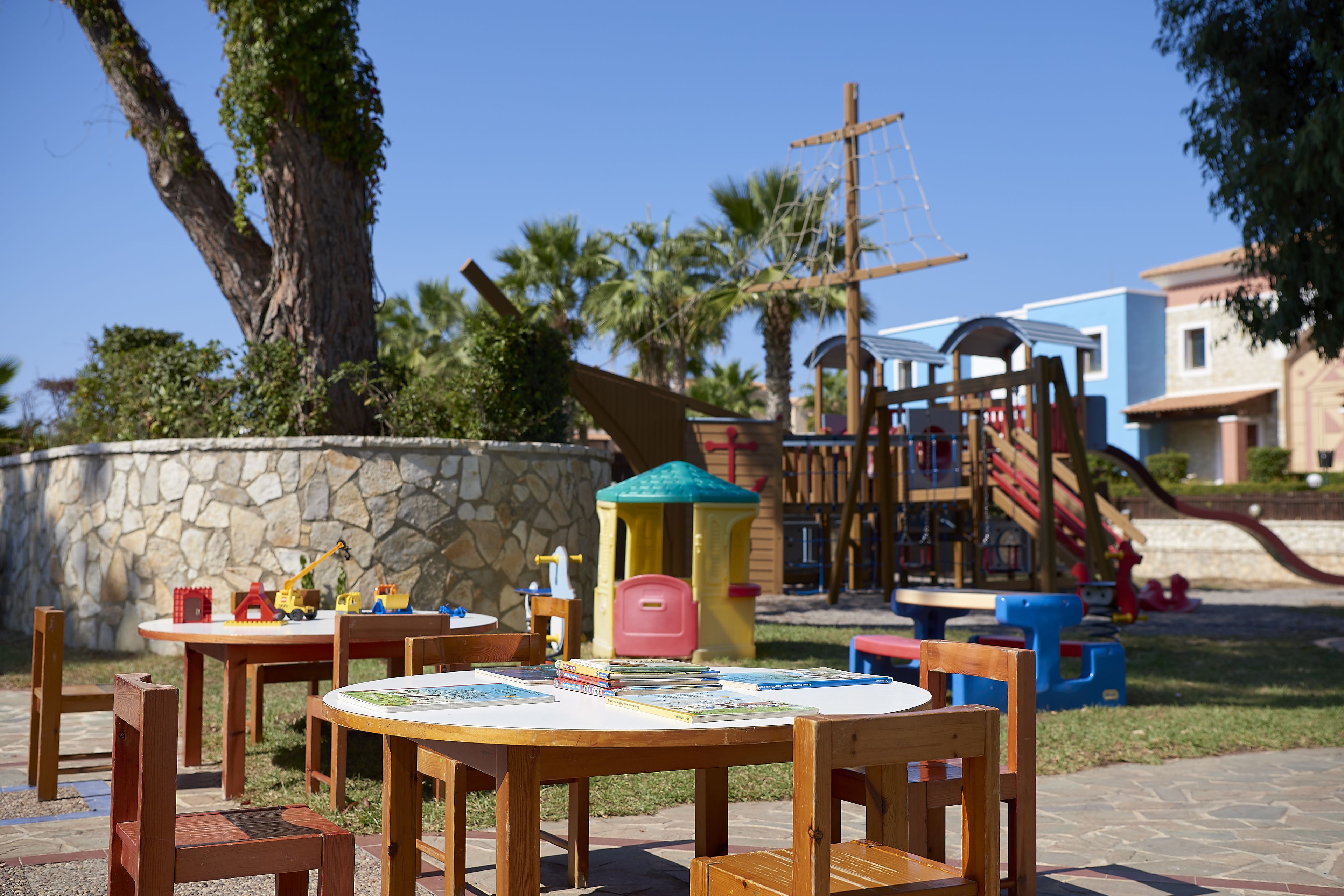 A wooden table with chairs and a play structure in the background.