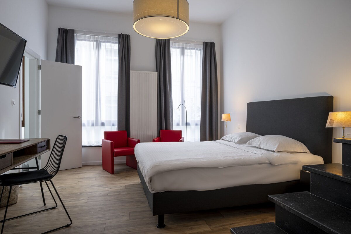 A modern hotel room with a bed, a desk, a chair, and a TV.